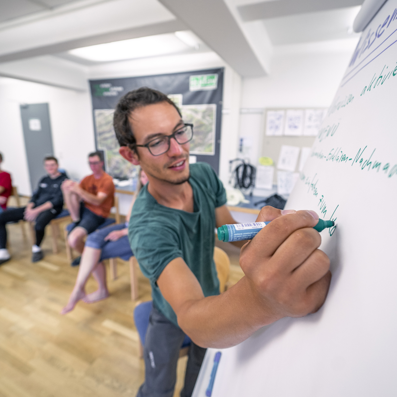 Leiter schreibt auf ein Flipchart. Im Hintergrund Kursteilnehmende.