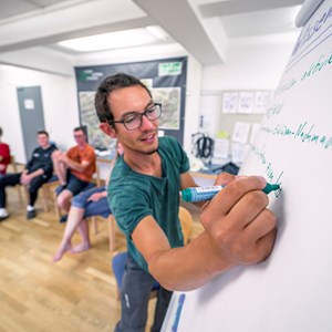 Leiter schreibt auf ein Flipchart. Im Hintergrund Kursteilnehmende.
